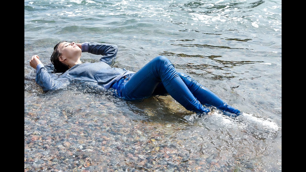 young beautiful girl tenderly poses in wet clothes on the ocean shore for wetlook video