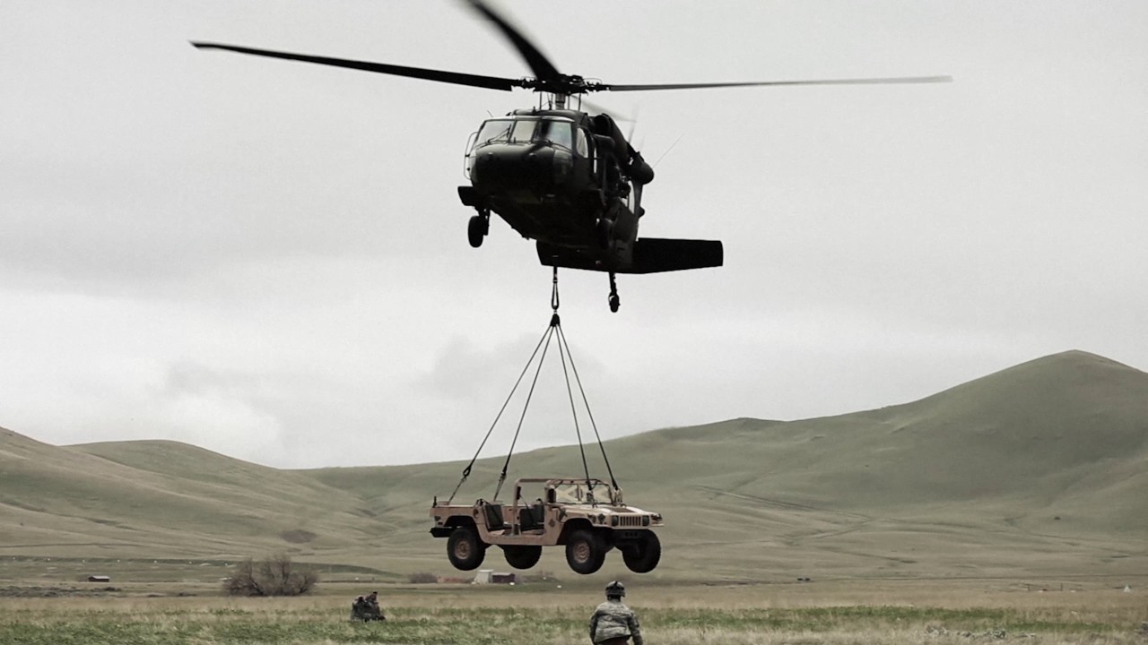 Shot from ground of Black Hawk helicopter lifting Humvee.
