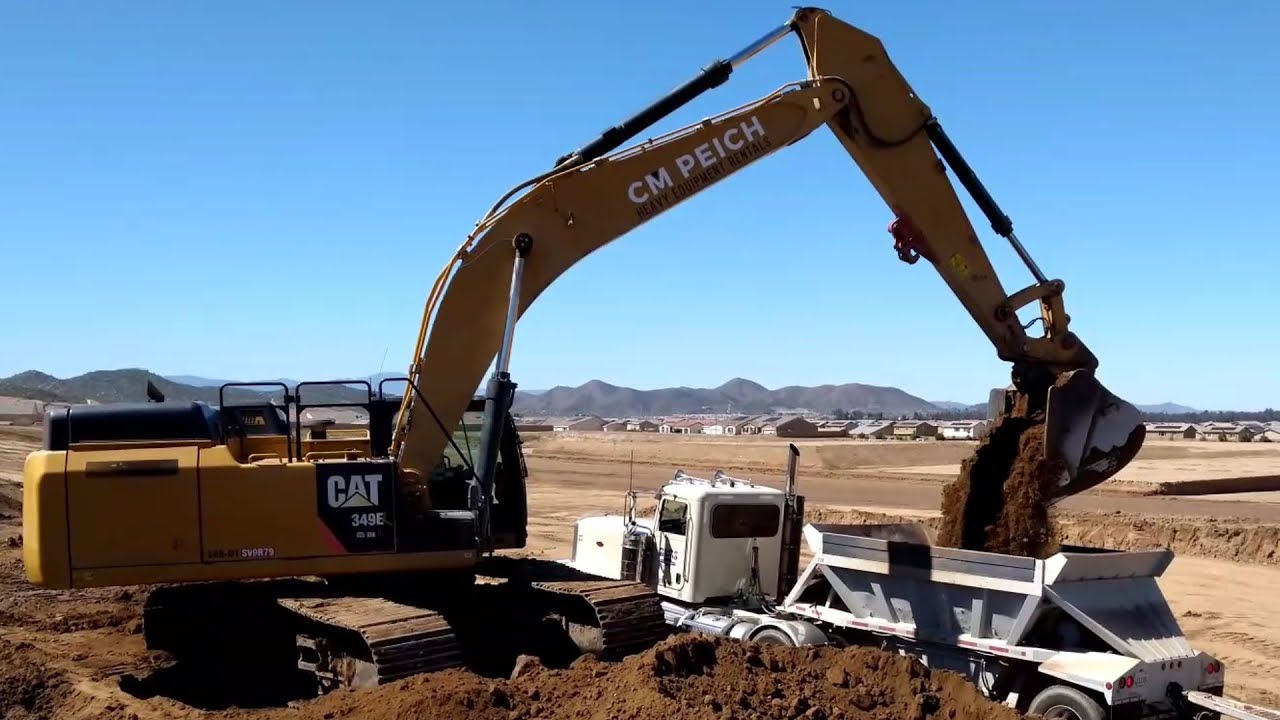 CAT 349E excavator loading belly dump trucks with four passes
