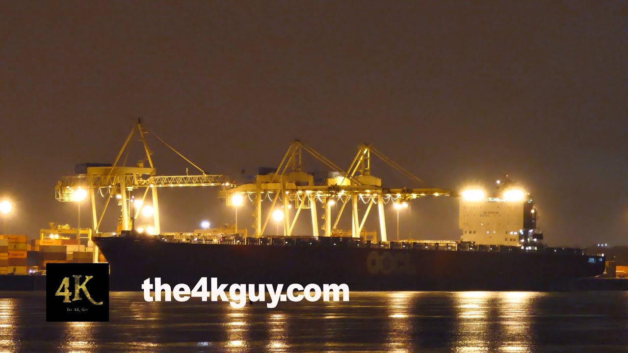 4K UHD - Huge cargo ship at night with cranes lifting containers in port
