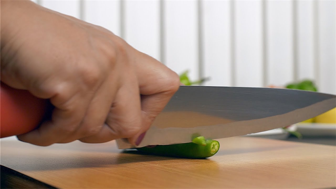 Woman using a knife to cut spicy green chili on cutting board  | Indian Stock Footage | Knot9