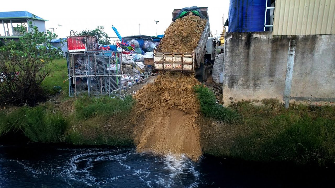 Dump Truck Unloading Dirt In the deep pit behind​ lake Trash to building with bulldozer