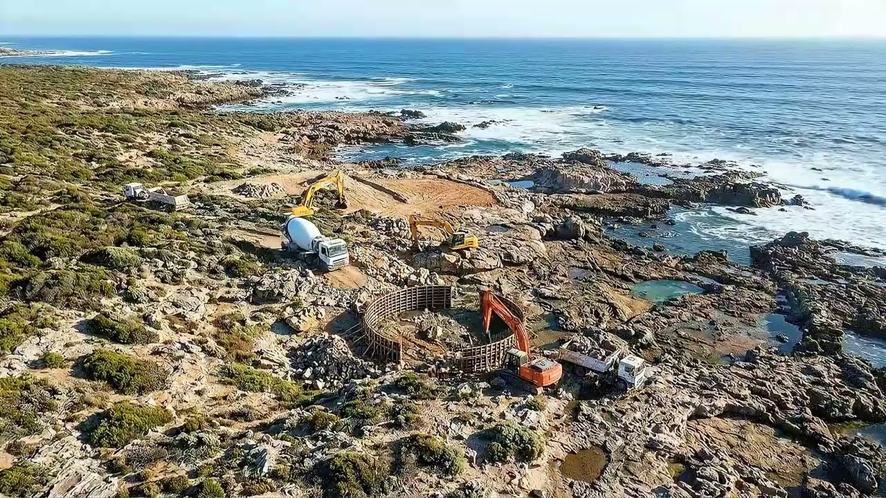 Coastal lighthouse complex on rocky shoreline, tall cylindrical tower with auxiliary buildings.