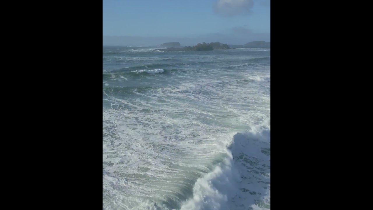 Waves roll into Cox Bay, Tofino on a clear day. Frank Island and Chesterman Beach in the distance