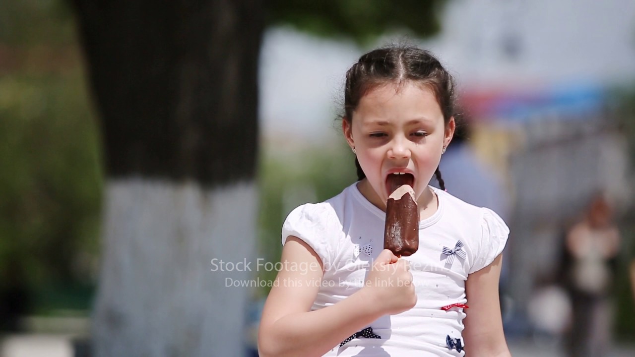 Close-up of cute little girl eating ice cream in park in sunshine summer day.