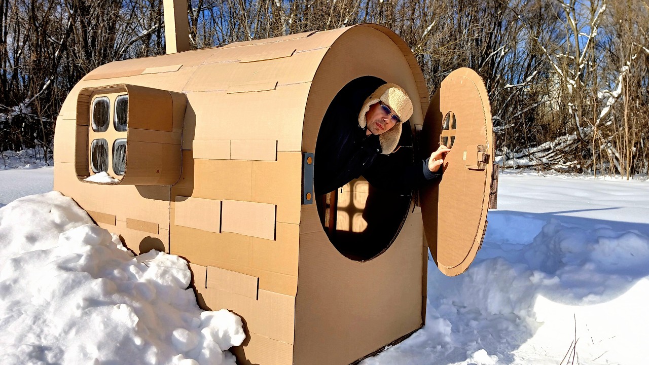 Man builds a small hobbit house out of cardboard and snow in a winter forest
