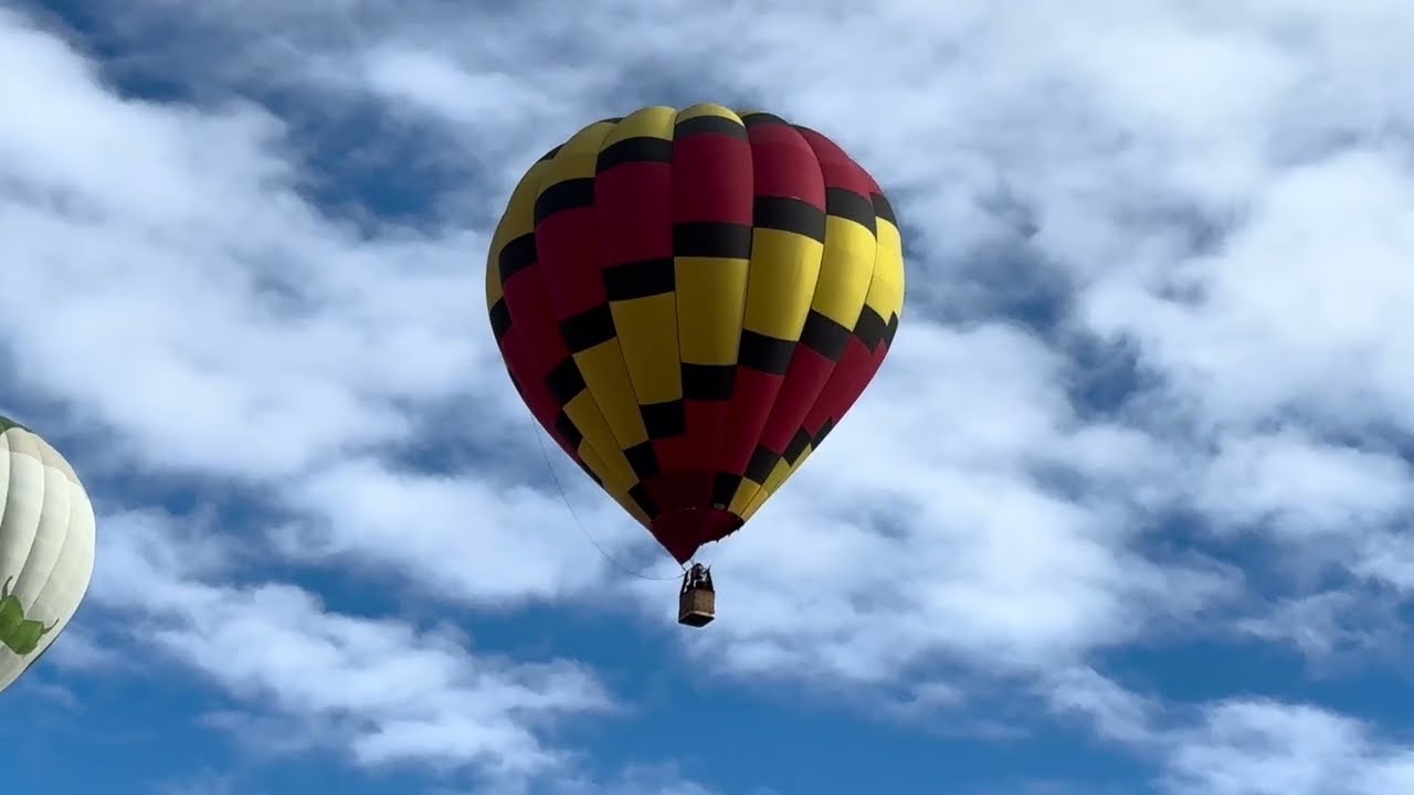 Red black & yellow floating next to green & white hot air balloon
