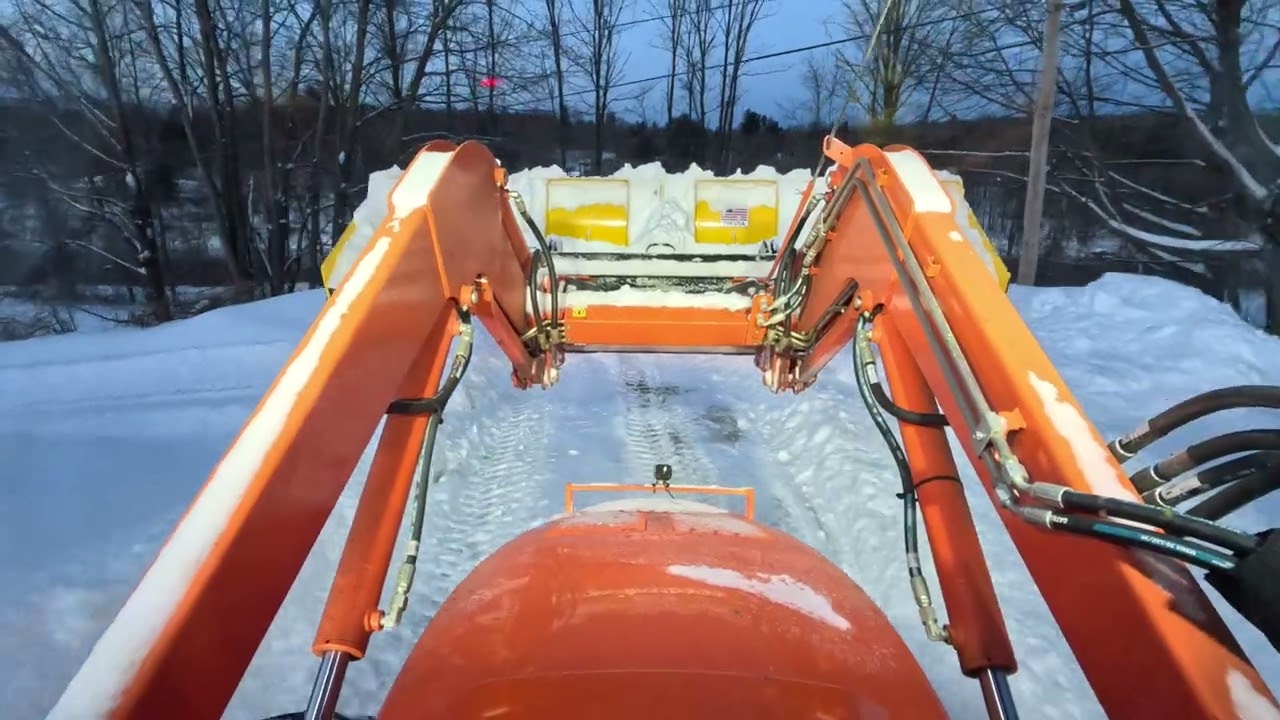 Snow plowing commercial parking lots with tractor.