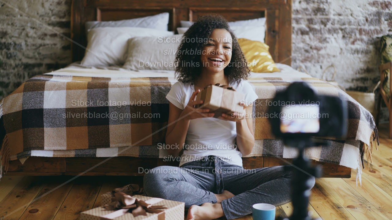 Young cheerful african american girl recording video blog about packing christmas gift box at home