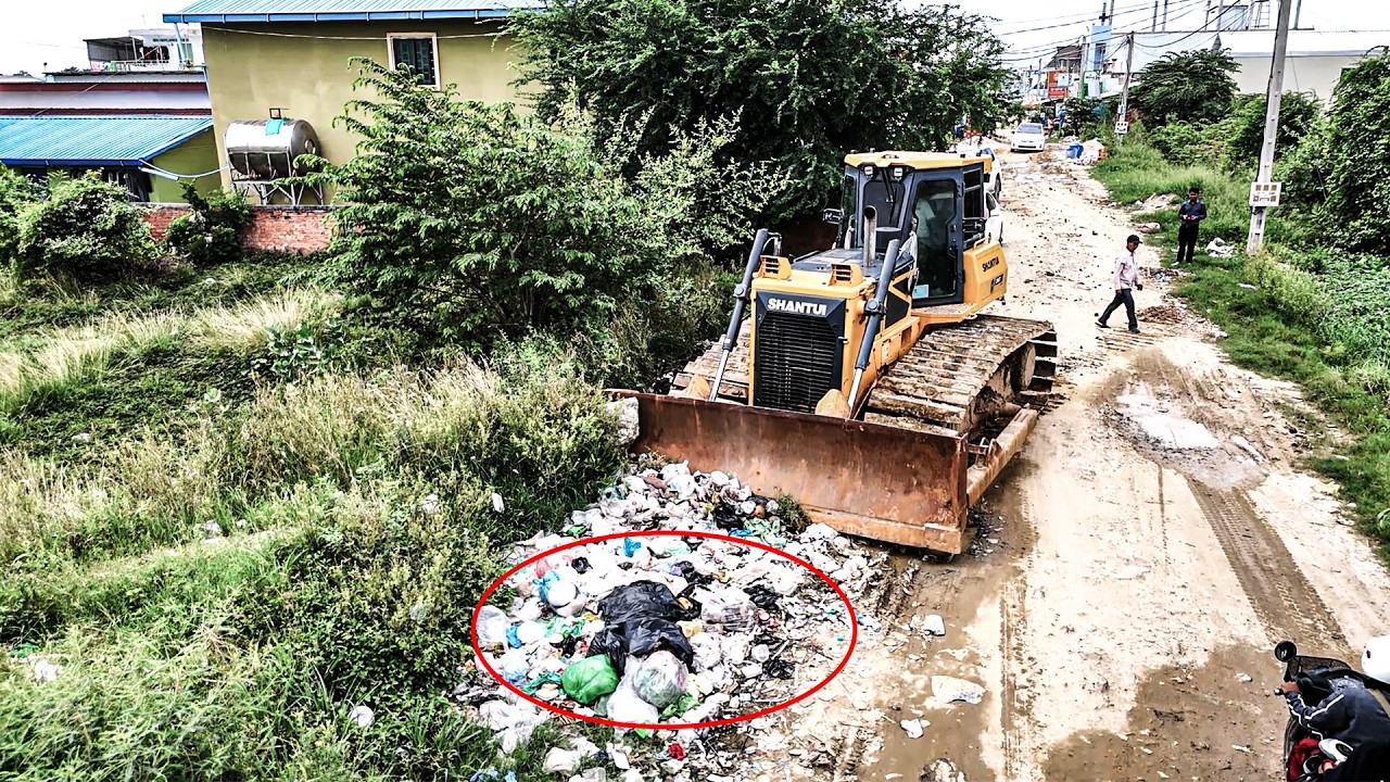 Bulldozer clears garbage and pushes soil filling land with dump trucks 