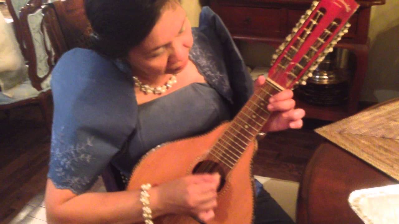 A Filipina Lady Playing a Filipino Musical Instrument In a Traditional Filipina Dress