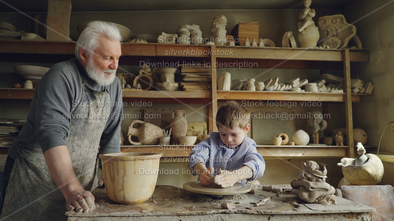 Small boy is molding clayware in his grandfathers's studio while his caring senior grandpa is