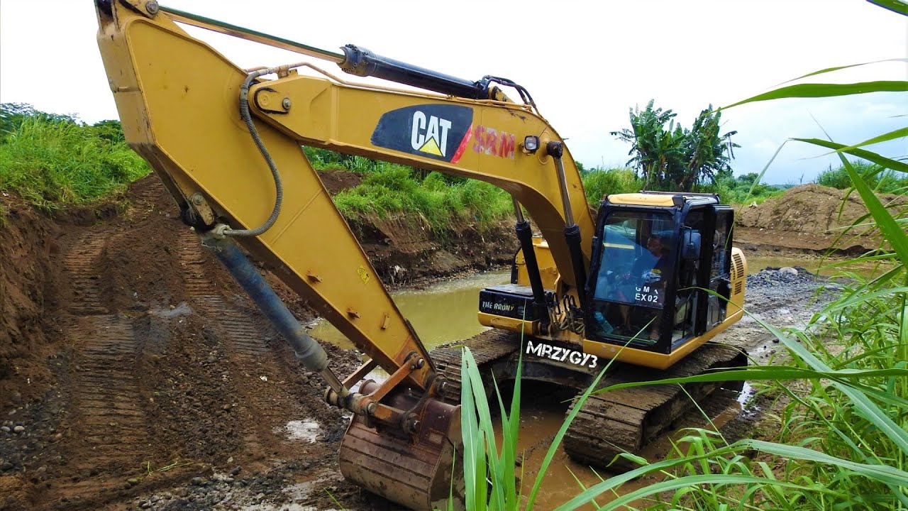 CAT 320D Excavator Digging Loading Sand And Rocks From The River Into Dump Trucks