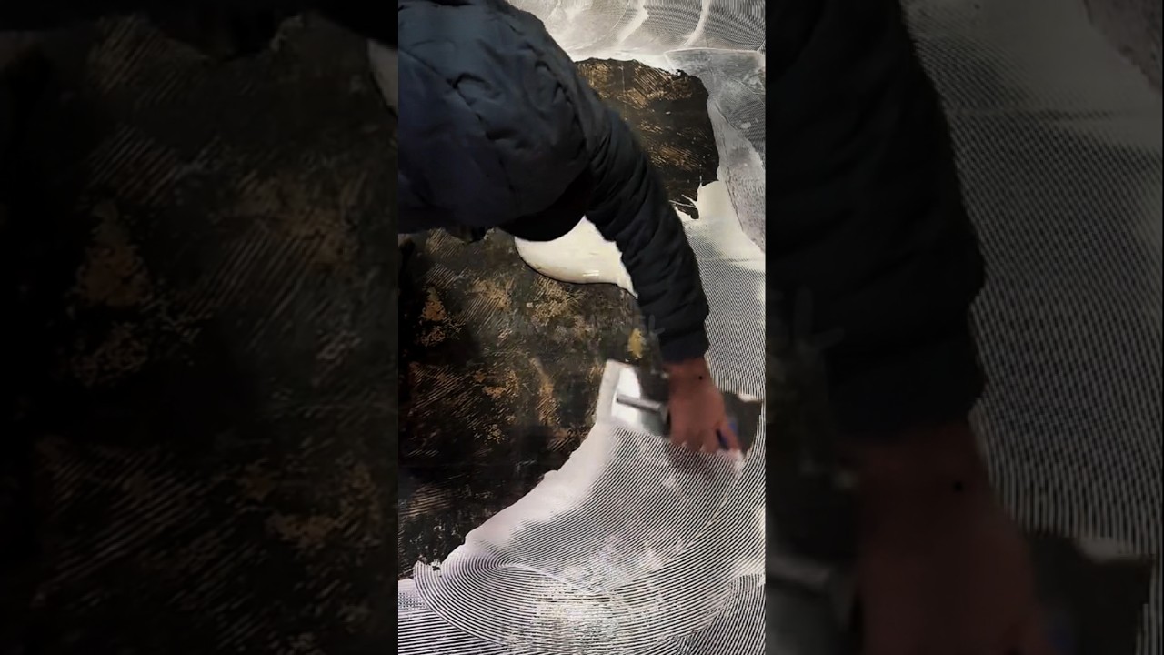 Рабочие наносят клей на пол с помощью зубчатой ​​кельмы. 