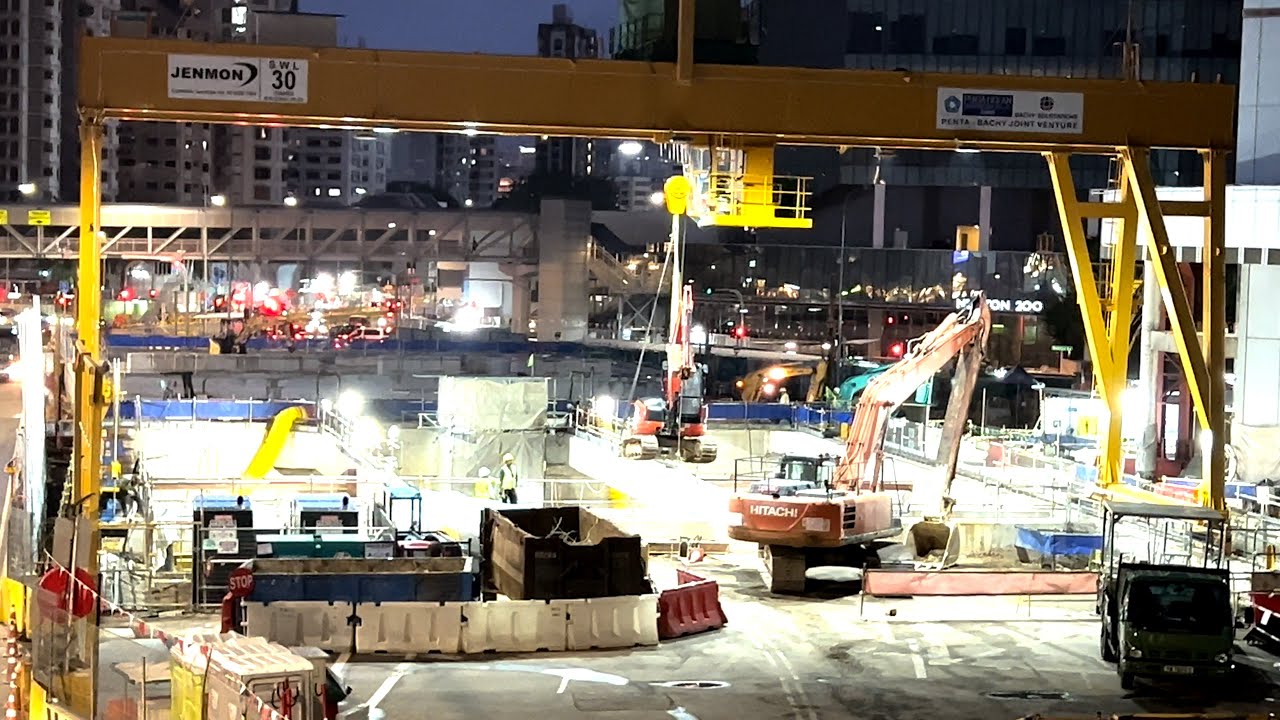 Gantry crane lifts excavator and places it underground AT NIGHT