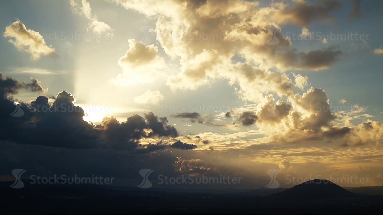 Rain clouds at wild field at spring. Sun's rays breaking through the clouds. Time lapse