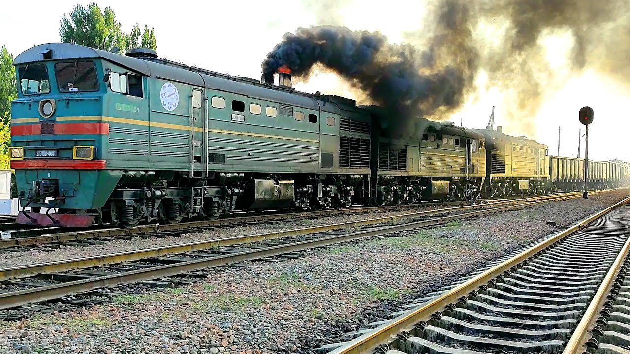 Diesel locomotive 2TE10V-4661 with a freight train, fire and black smoke covers the sky.