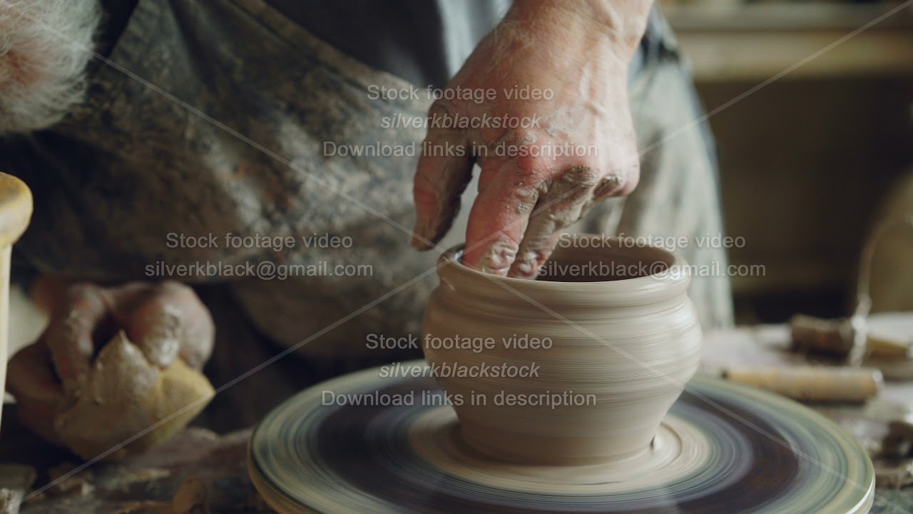 Professional potter is making clayware on potter's wheel, looking at half-finished pot and checking