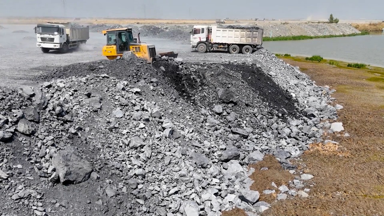Fantastic!! Bulldozers and dump trucks are working together to dump rocks into the lake