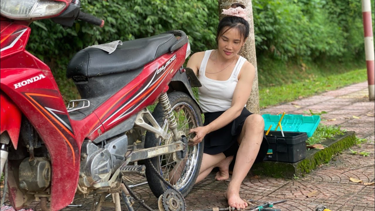 The girl fixed a beautiful girl's Honda motorbike that had a flat tire in the middle of a slope.