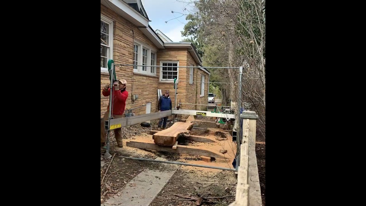 Cutting slabs with the Lucas Mill. Narrow alley between building and a fence.