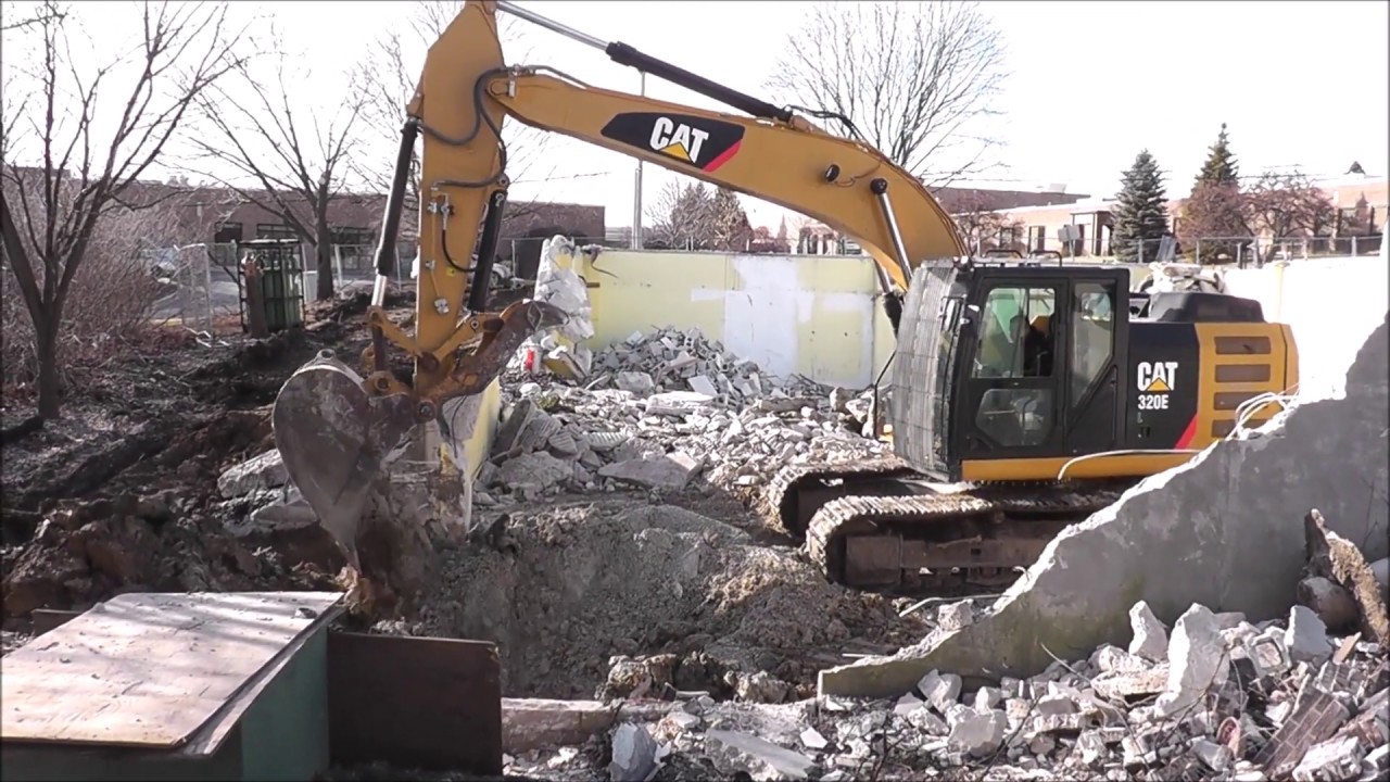 CAT 320 excavator breaking an old building foundation