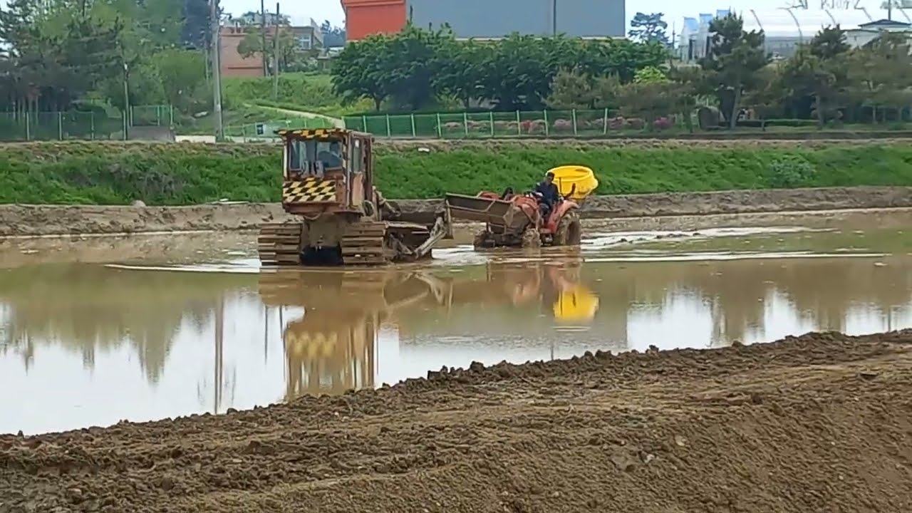 A tractor stuck in a field is dug out by a bulldozer.