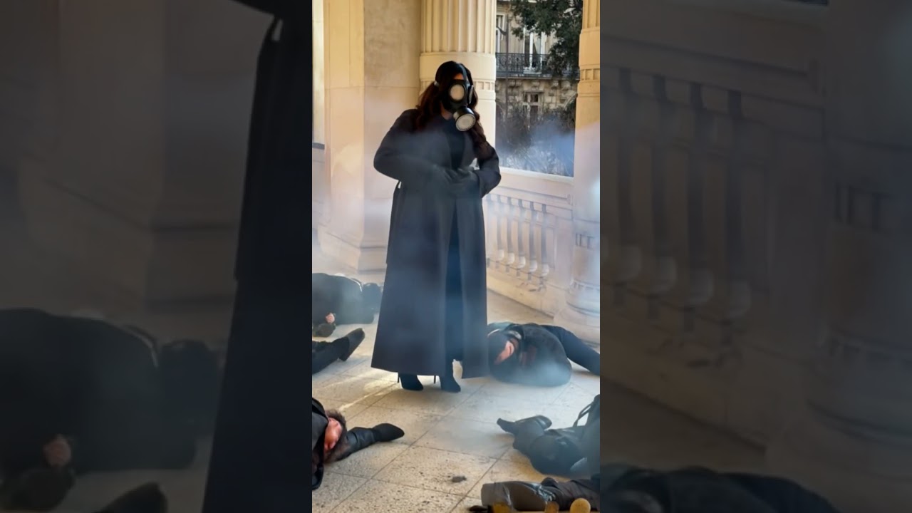 woman in trenchcoat and gasmask checks her enemies are dead