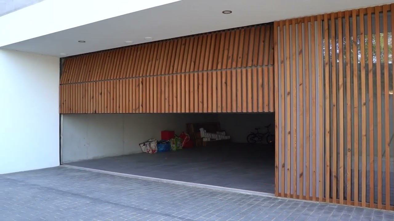 Fachada com portão seccionado e porta pivotante revestida com ripado de madeira