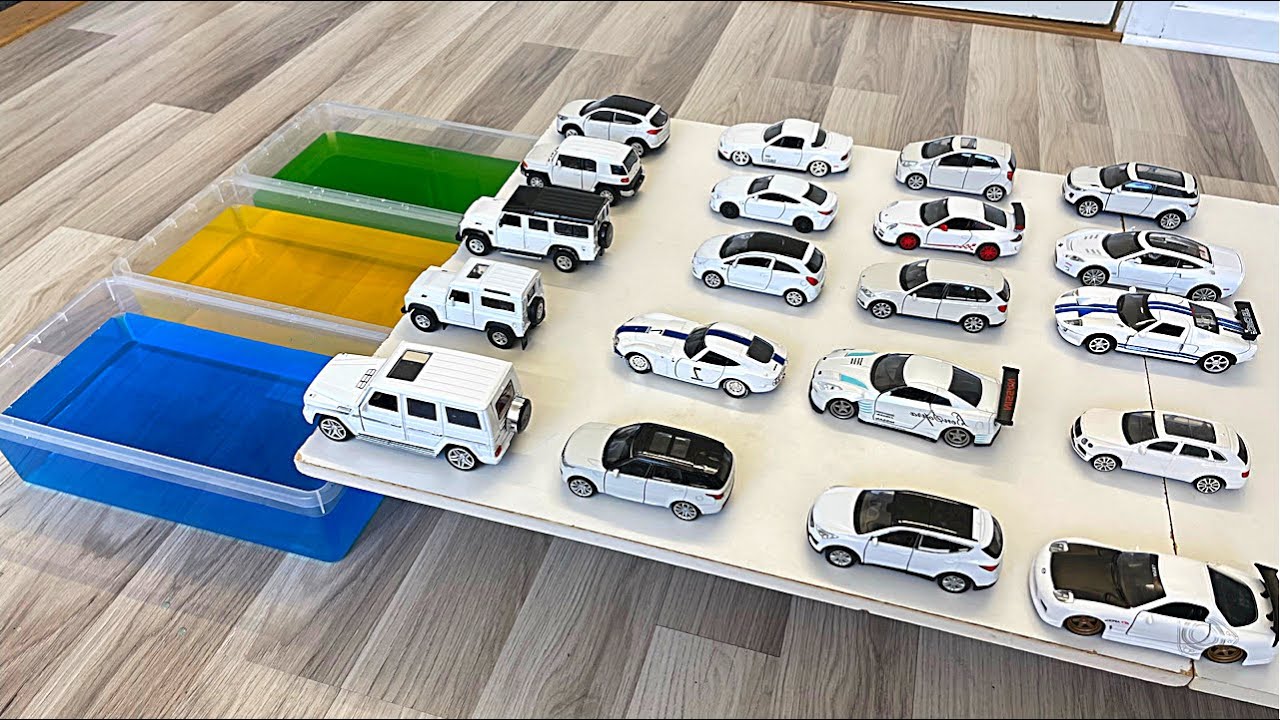 Various White Diecast Model Cars Sliding Into The Green, Blue And Yellow Water