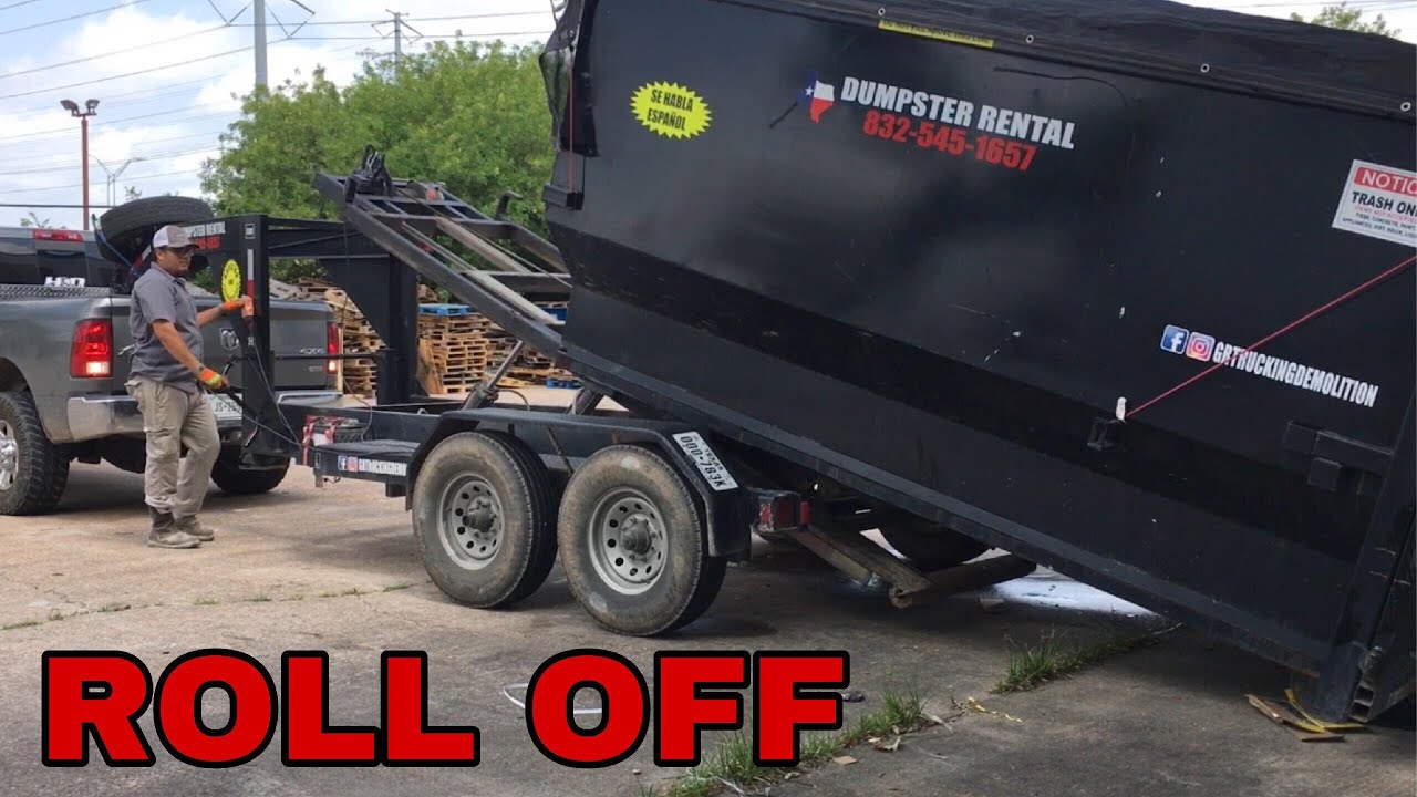 Gooseneck roll off dump trailer loading a heavy dumpster