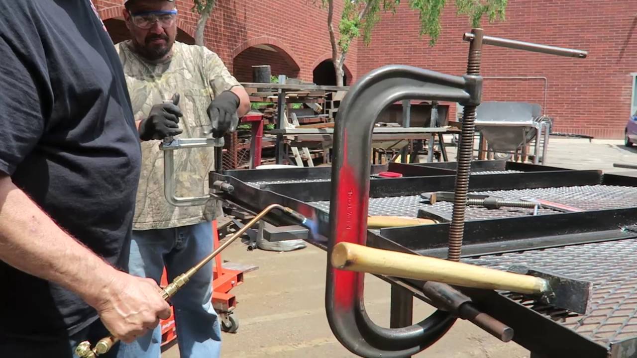 Repairing a bent trailer gate with hammers, clamps, fire, and welds.