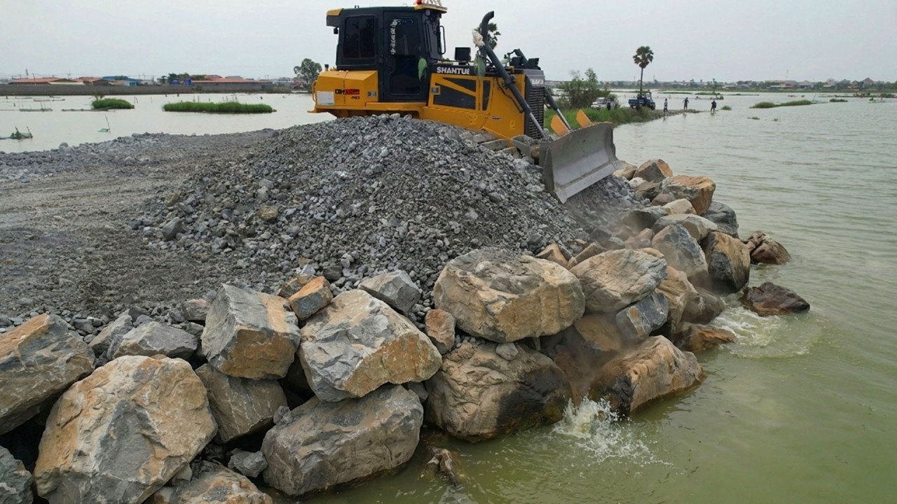 Pushing stones into the lake to release water By ozer SHANTUI C3 Push Stone And DumpTruck10Wheel
