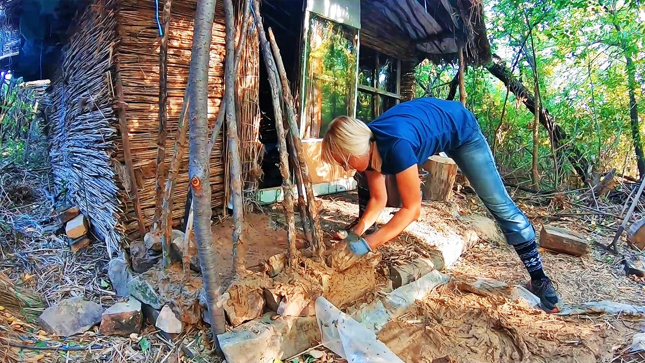 Woman builds a reed hut alone. A clay fireplace and wall insulation