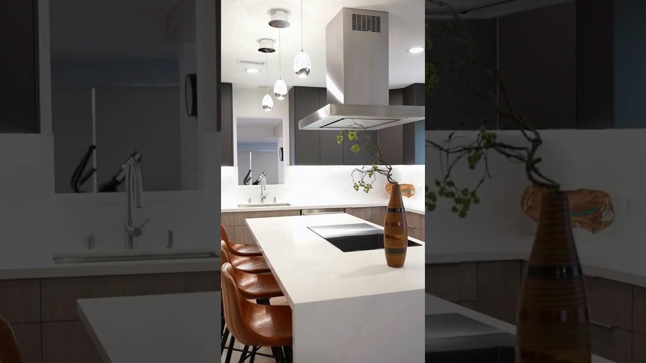 Two tone European slab door cabinet kitchen with a waterfall island, pendant lights and island hood