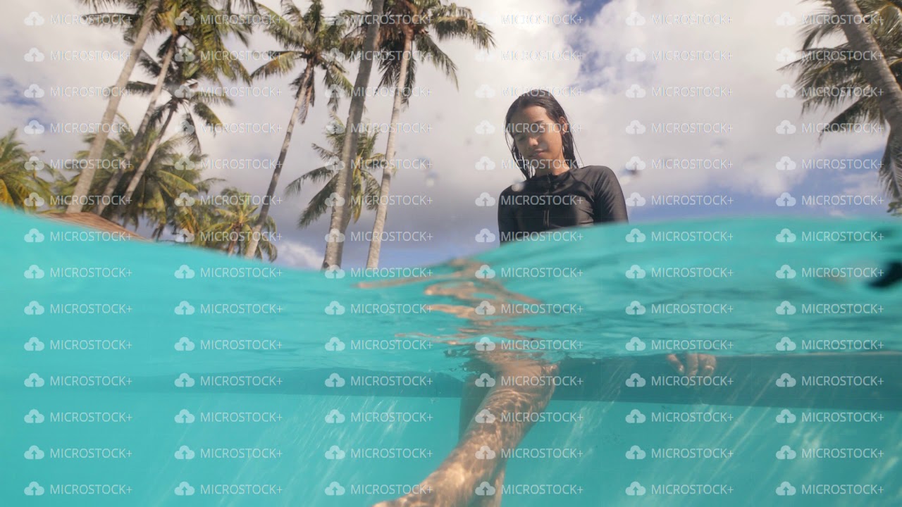 Beautiful asian girl splashing water sitting on the edge of pool in tropics.