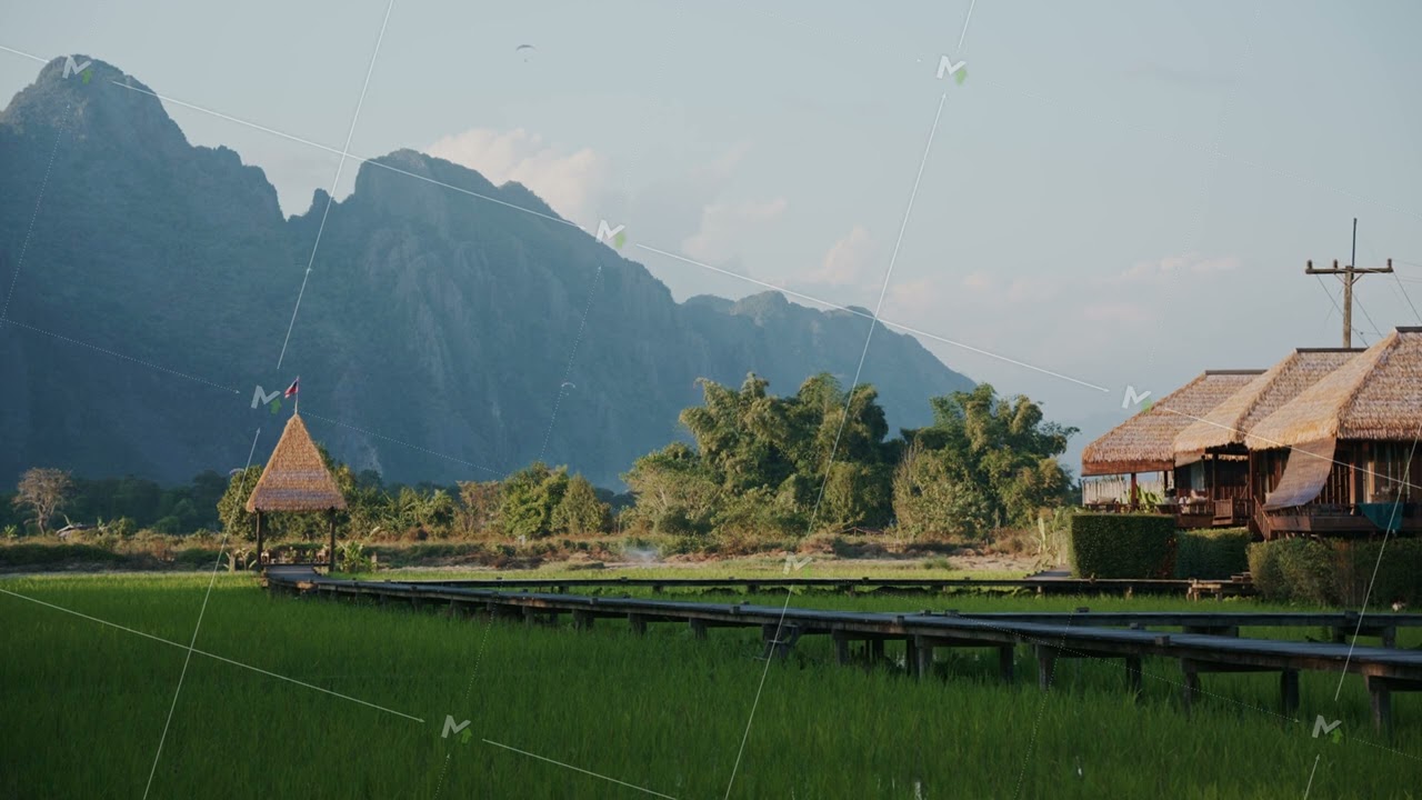 Scenic Laos rice paddy landscape with bungalows, wooden boardwalk and karst mountains in remote