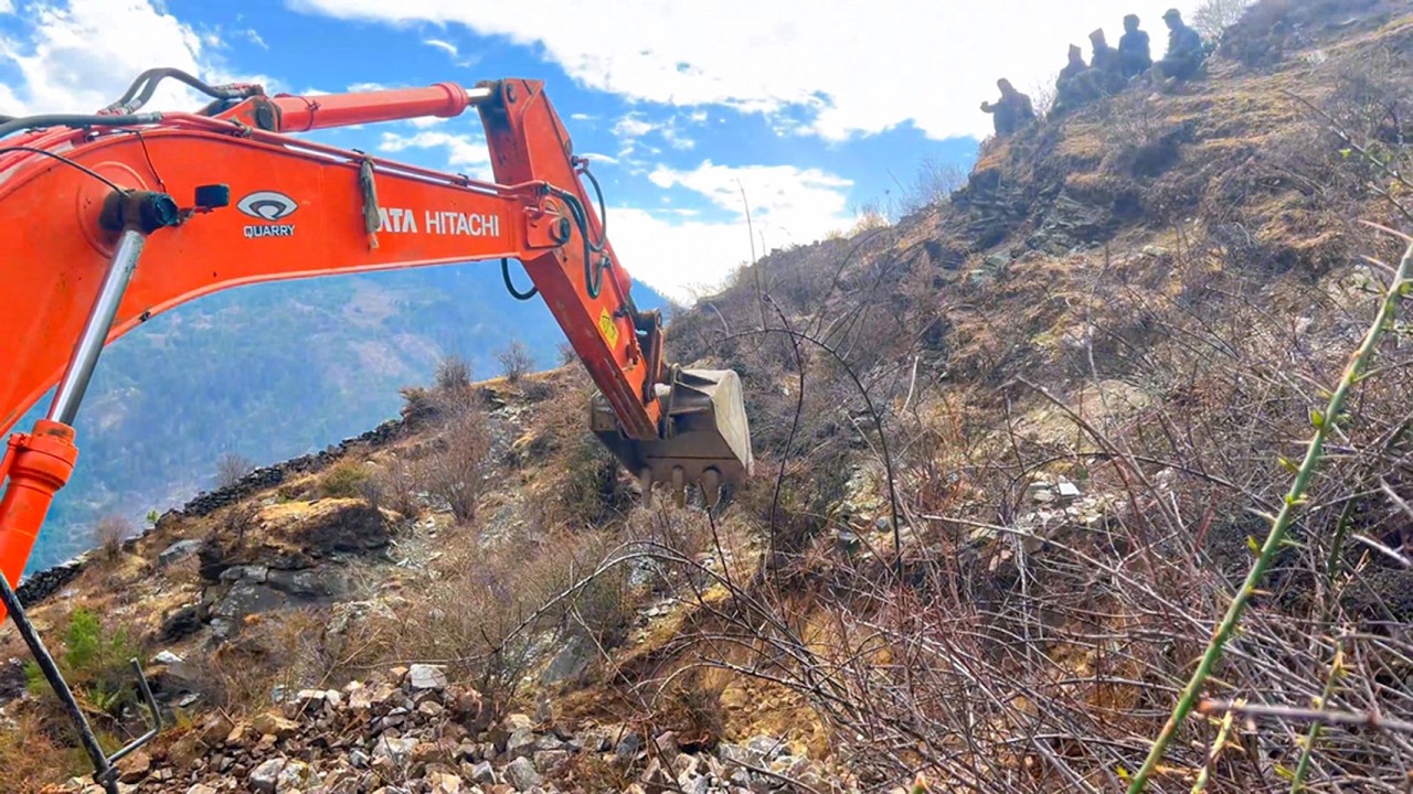 Expert Operator Building Narrow Mountain Road: Excavator Expertly Clears Stones and Trees.