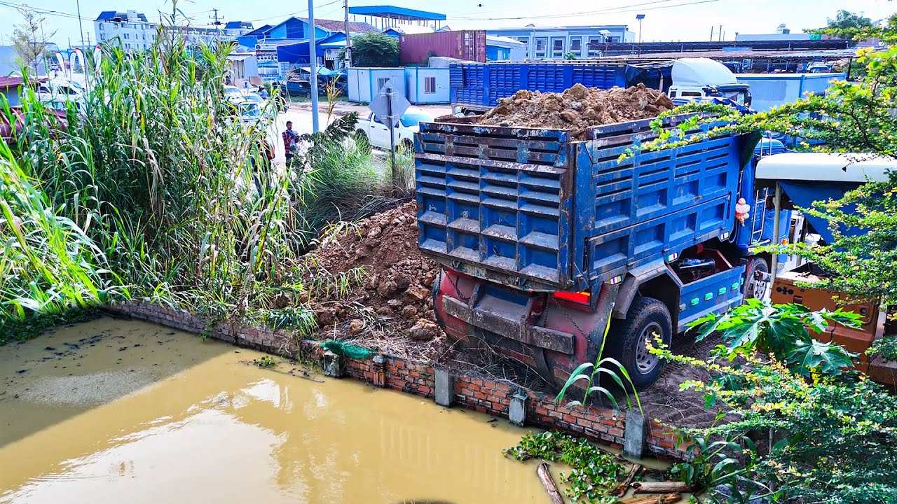 Nice skill bulldozer operator pushes soil filling up land with dump trucks unloading dirt