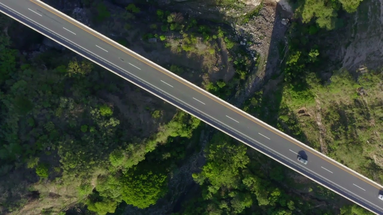 A tranquil aerial view of two cars traversing a scenic bridge surrounded by lush greenery. #4kvideo