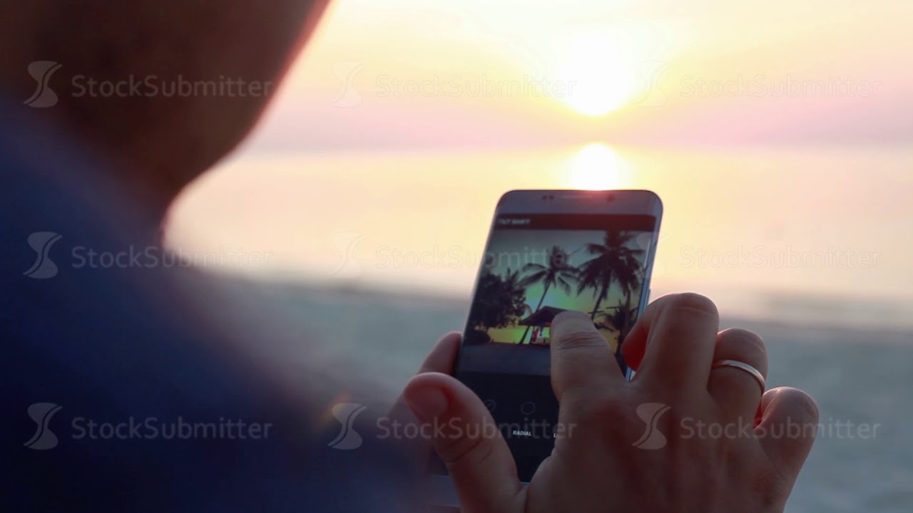 Handsome man resting at the bar on the beach uses mobile phone during beautiful sunset. Man is