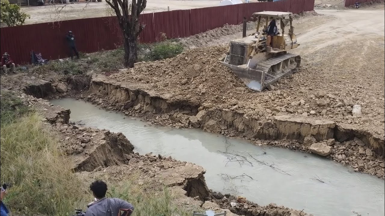 An Old Strong Komatsu Dozer Pushing Soil And Rock Filling Land With 25T Dump Trucks
