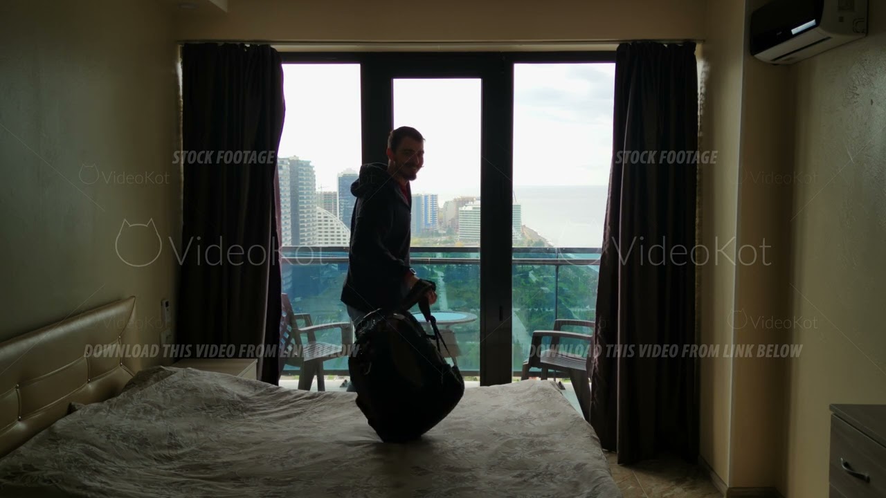 Slow motion of male tourist opening curtains in hotel room and enjoy view from balcony at coastline