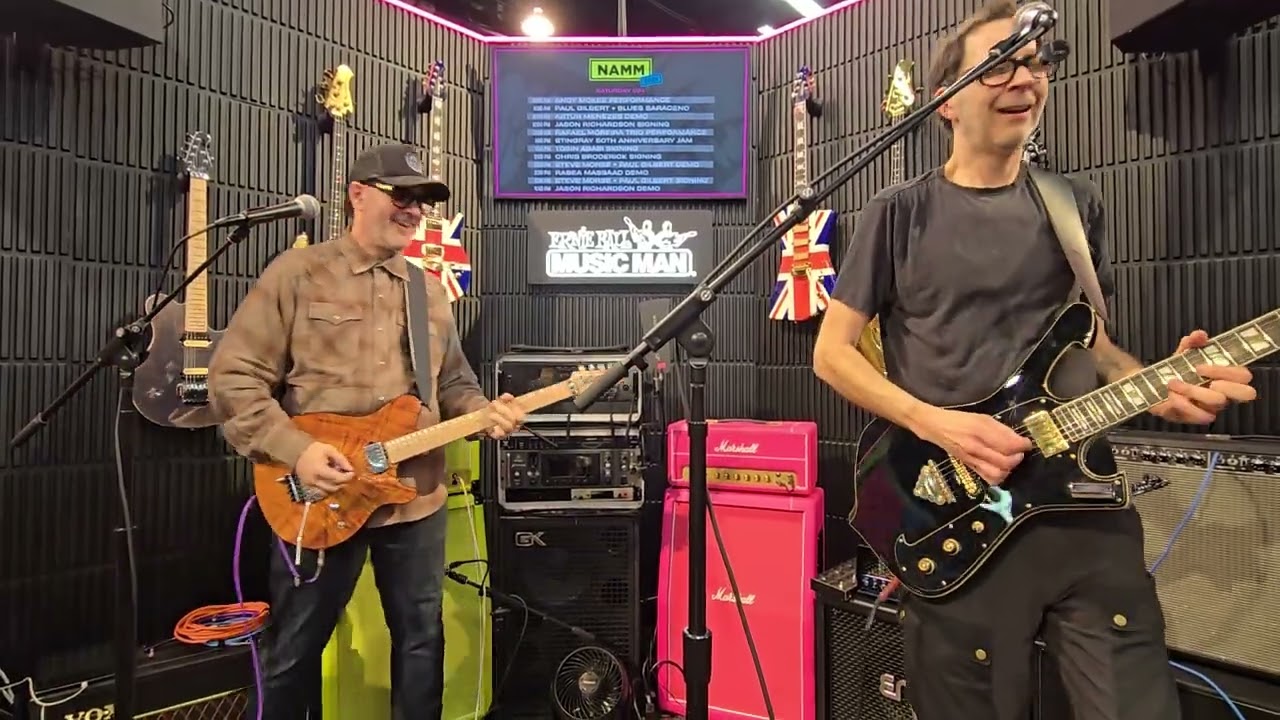 Игроки команды Blues Сарасино и Пол Гилберт исполняют песню Going Mobile. Выставка NAMM 2026.