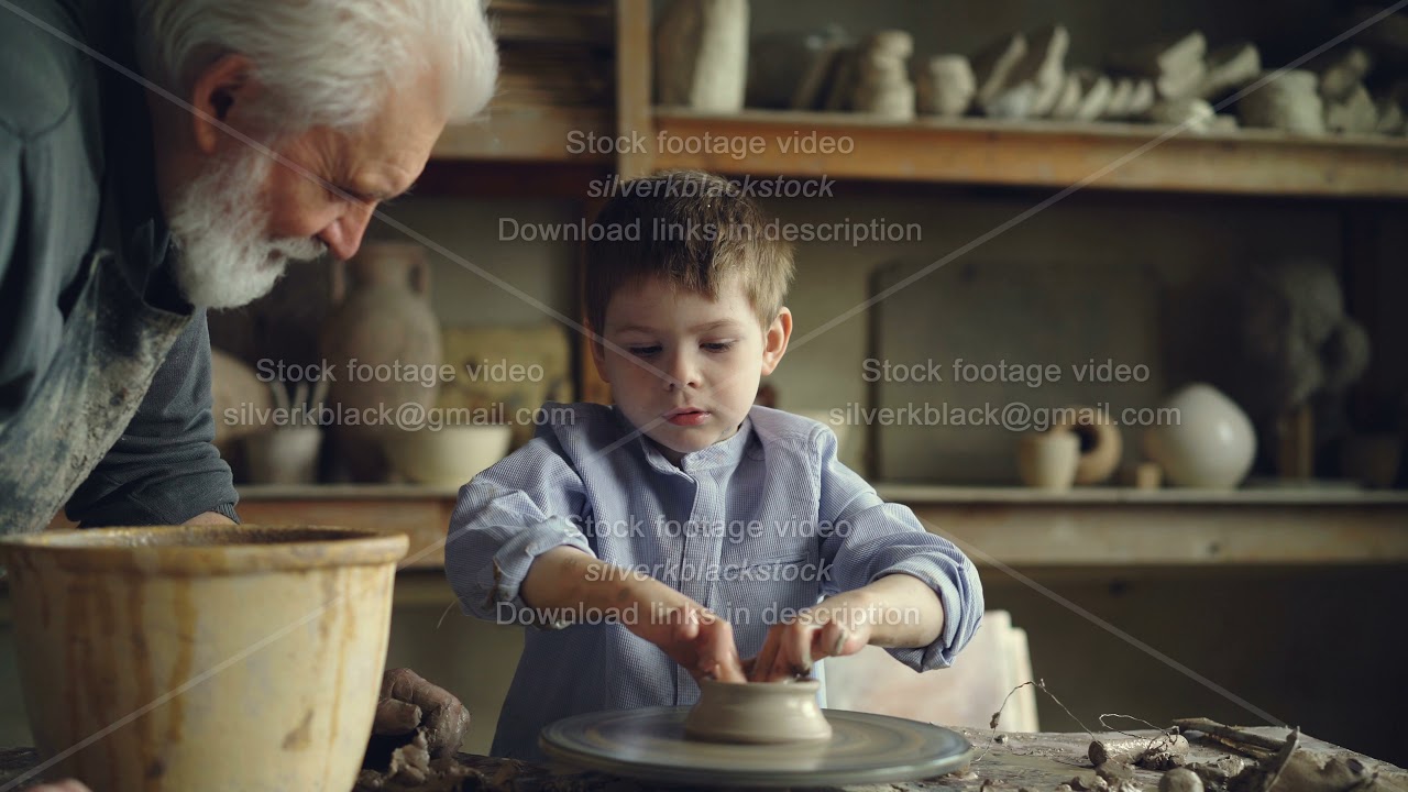 Little boy pottery learner is creating clayware on throwing-wheel while his experienced grandgather
