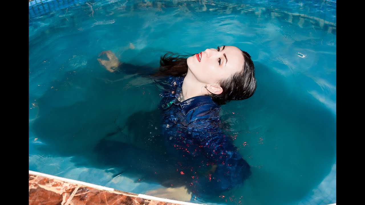 cute girl in wet denim jacket and wet jeans poses tenderly in swimming pool for wetlook video