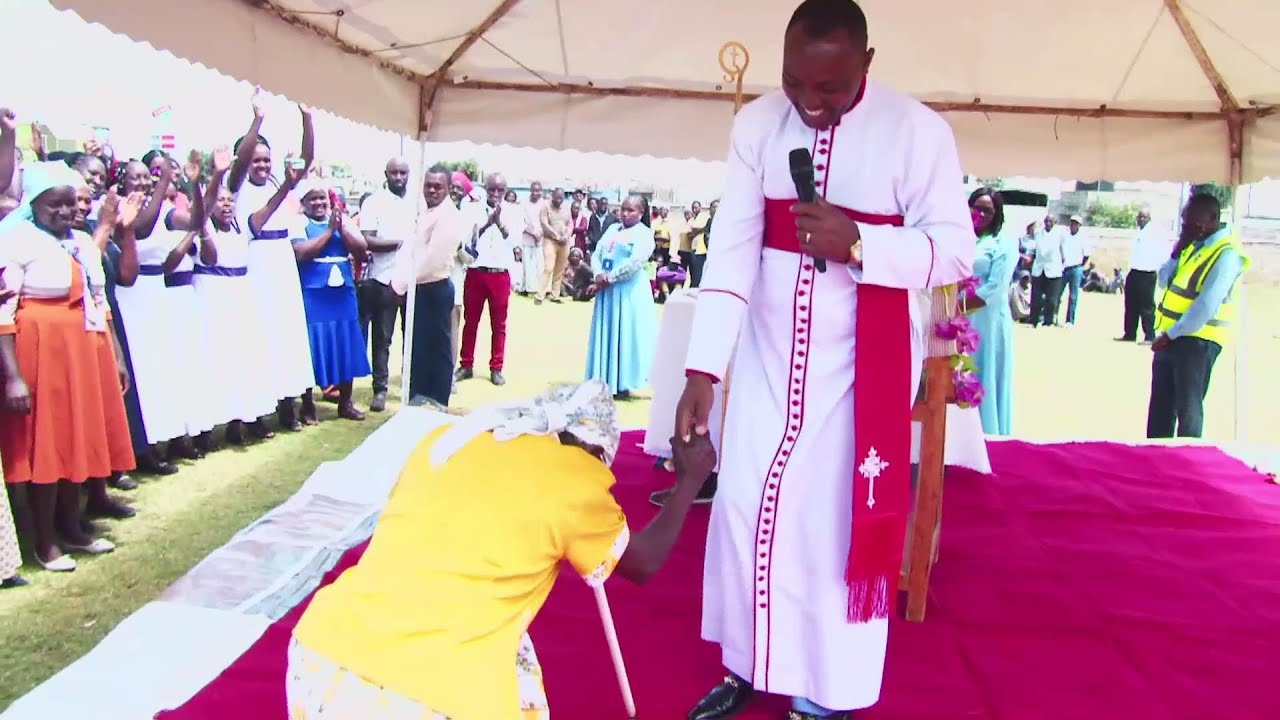 Bishop Ben Helps Woman Dancing with Sticks with money  During Ordination Ceremony in Laikipia County