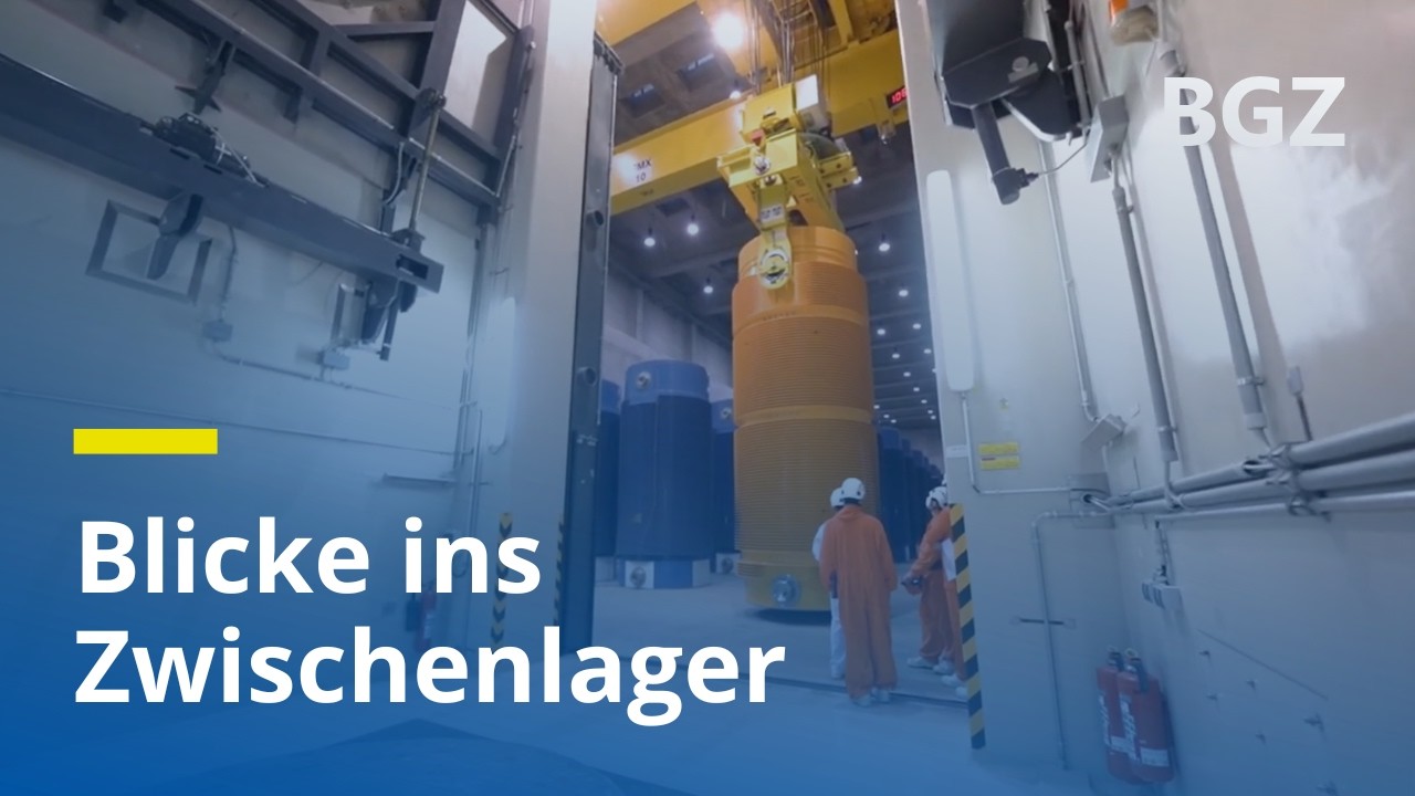 Blick in ein Lager f&uuml;r hochradioaktive Abf&auml;lle: Mitarbeitende stehen vor CASTOR-Beh&auml;lter am Kran