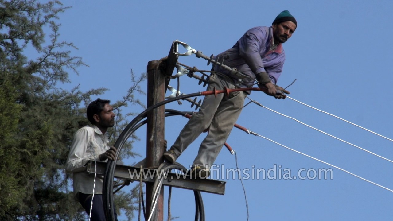 Dangerous work: standing atop electricity poles and changing cables in India