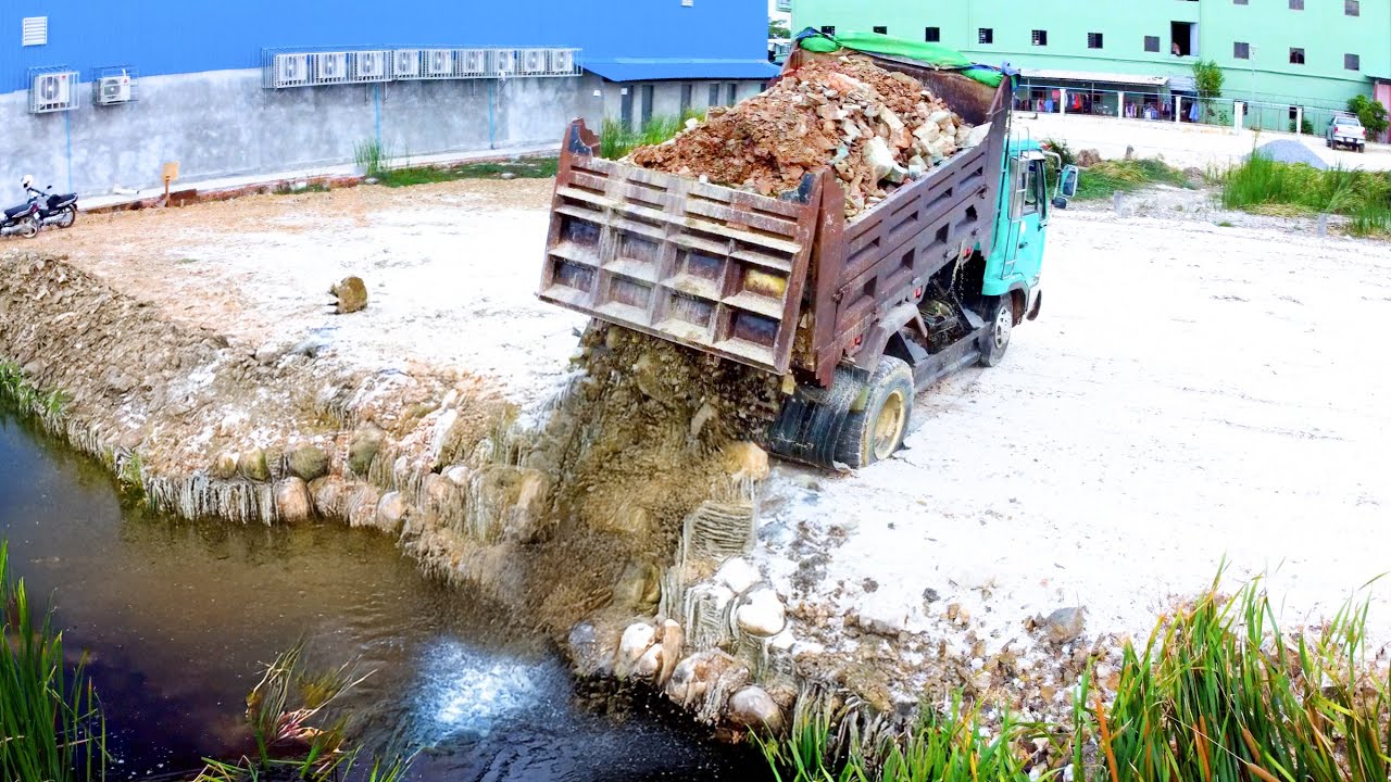 Complete the project dump truck unload rock into the flood pushing by bulldozer KOMAT'SU D20P